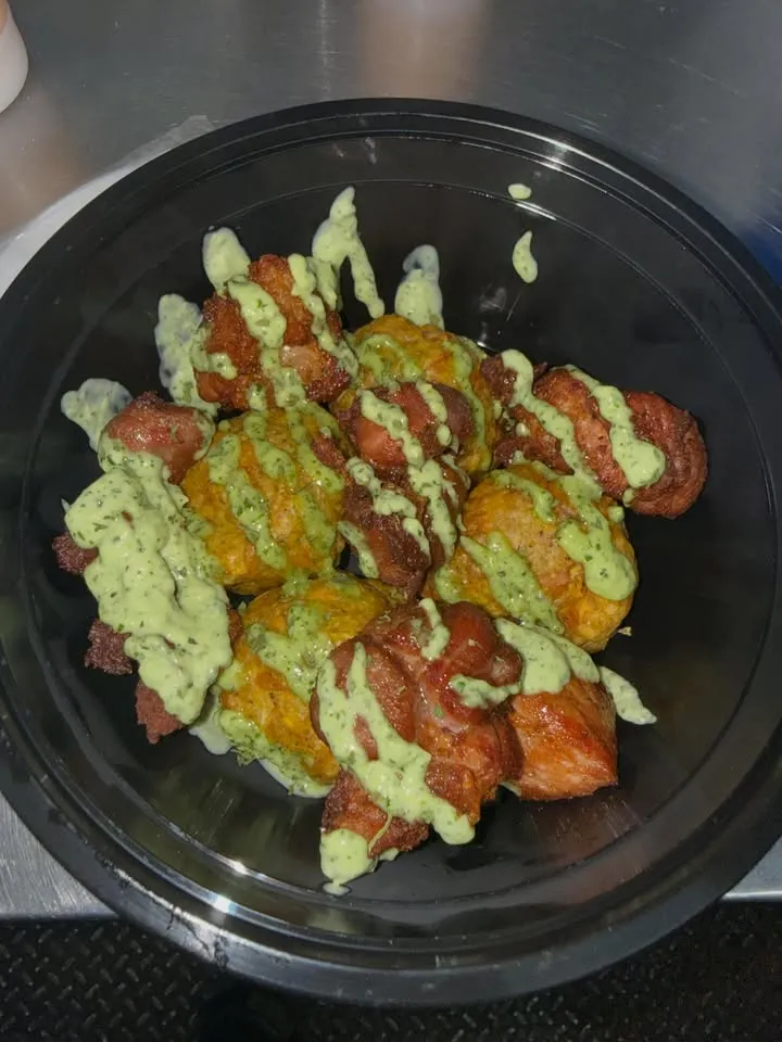 A bowl of meat with a green drizzle sauce.
