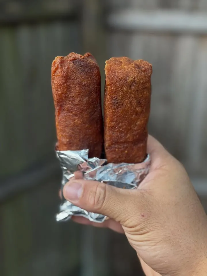 Two fried rolls wrapped in foil, held in a hand.