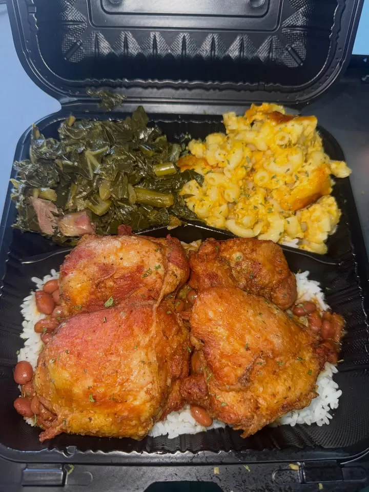 A takeout box with fried chicken thighs over rice, with collard greens and mac and cheese.