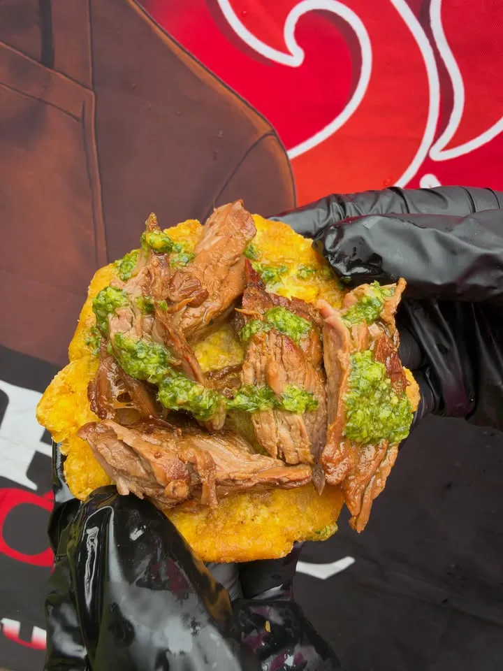 A fried tostón topped with pulled pork and a green sauce.