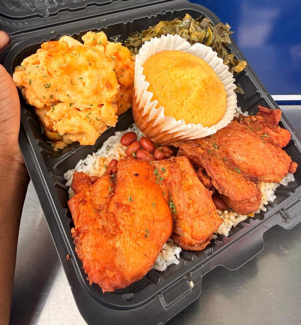A black takeout box with fried chicken chicharrón, white rice with red beans, mac and cheese and collard greens.